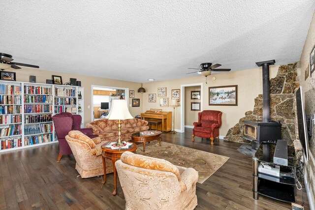 living room with hardwood / wood-style flooring, ceiling fan, a wood stove, and a textured ceiling