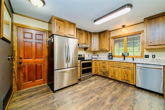 kitchen with crown molding, hardwood / wood-style floors, light stone counters, sink, and appliances with stainless steel finishes