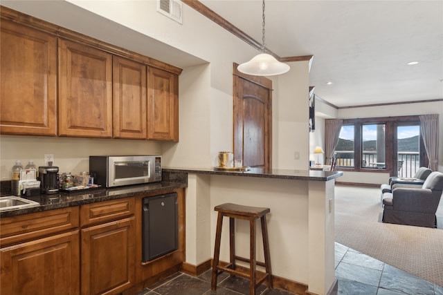 kitchen with kitchen peninsula, hanging light fixtures, crown molding, a kitchen bar, and dark colored carpet