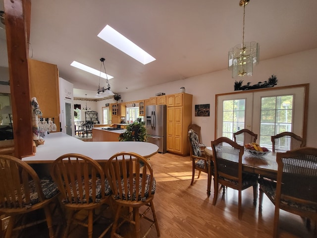 dining area featuring light hardwood / wood-style floors, french doors, vaulted ceiling with skylight, and an inviting chandelier