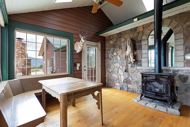 dining space with vaulted ceiling, hardwood / wood-style flooring, ceiling fan, and a wood stove