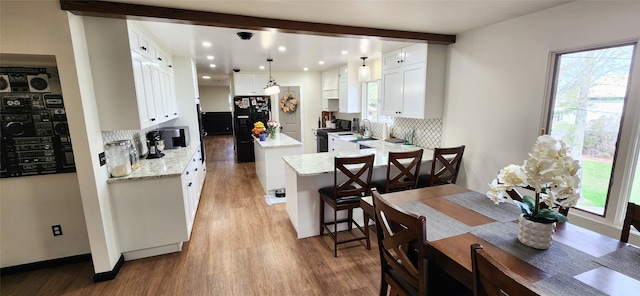 kitchen with white cabinetry, hanging light fixtures, black appliances, backsplash, and hardwood / wood-style floors