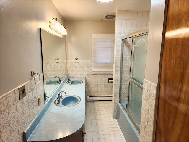 bathroom with tile walls, vanity, combined bath / shower with glass door, a baseboard heating unit, and tile patterned floors