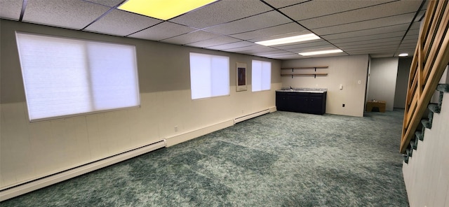 basement featuring a paneled ceiling, dark colored carpet, and a baseboard heating unit