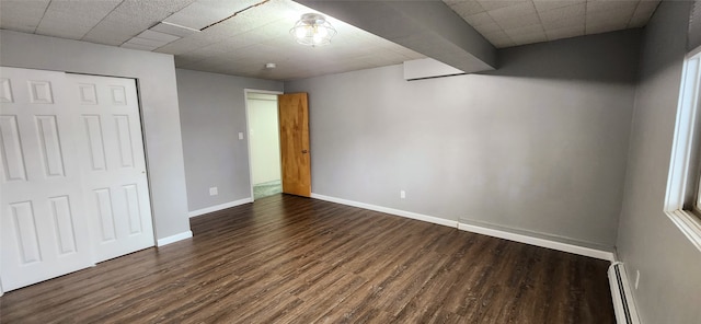 unfurnished bedroom featuring a baseboard heating unit, a closet, and dark hardwood / wood-style flooring