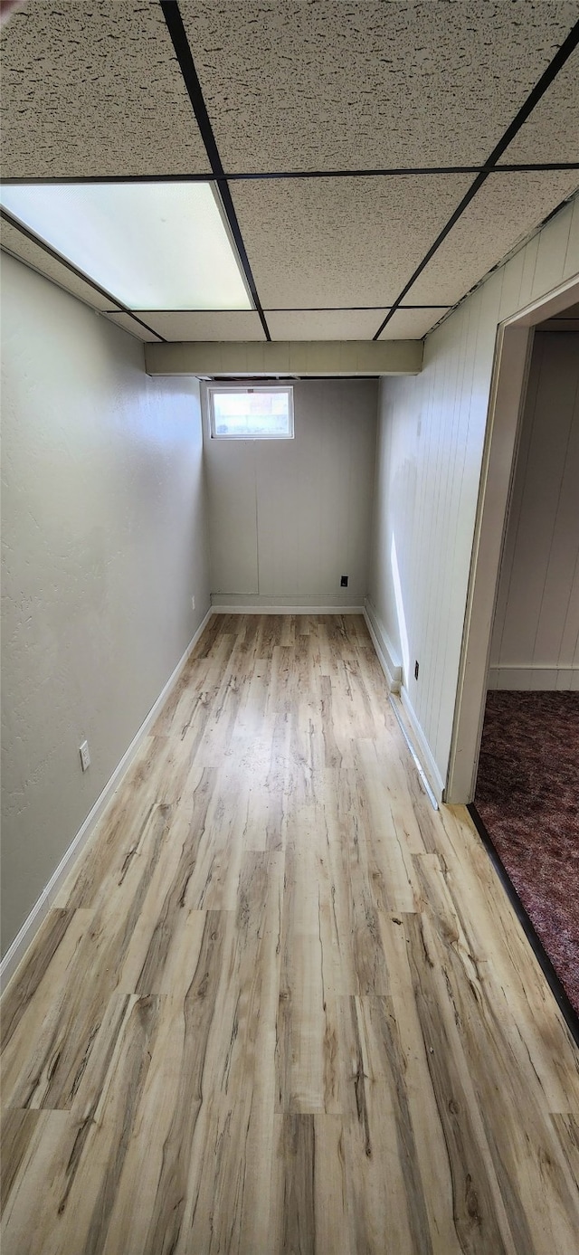 basement with light hardwood / wood-style floors, wooden walls, and a drop ceiling