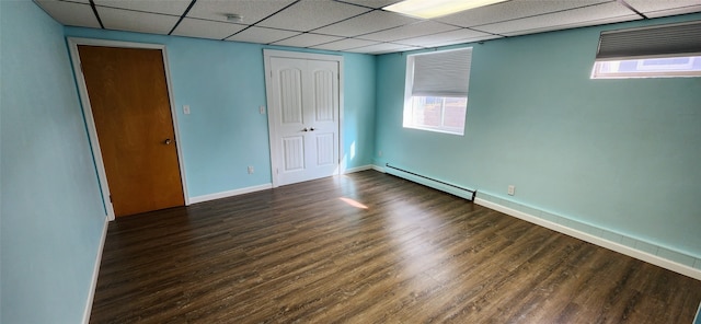 unfurnished bedroom with a baseboard radiator, multiple windows, a drop ceiling, and dark hardwood / wood-style floors