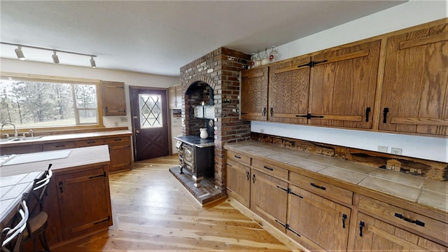 3653 Sophie Lake Rd, Eureka, MT 59917 - kitchen with a wood stove, light wood-style flooring, tile counters, brown cabinets, and rail lighting