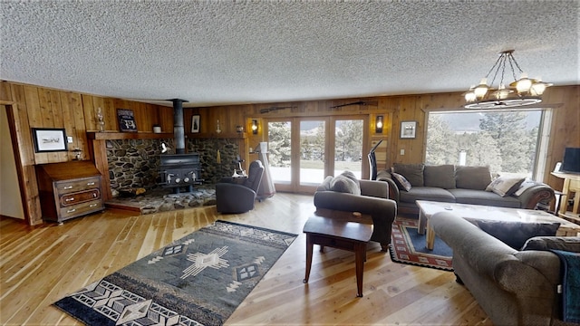3653 Sophie Lake Rd, Eureka, MT 59917 - living room featuring wood walls, a textured ceiling, a wood stove, a chandelier, and light wood-style flooring