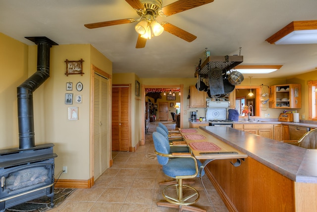 kitchen with a wood stove, light tile flooring, ceiling fan, a breakfast bar area, and sink