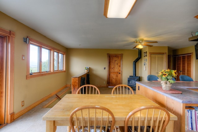 dining room featuring baseboards, a ceiling fan, a wood stove, and light tile patterned floors
