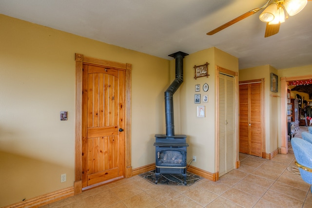 interior space featuring ceiling fan, a wood stove, and light tile floors