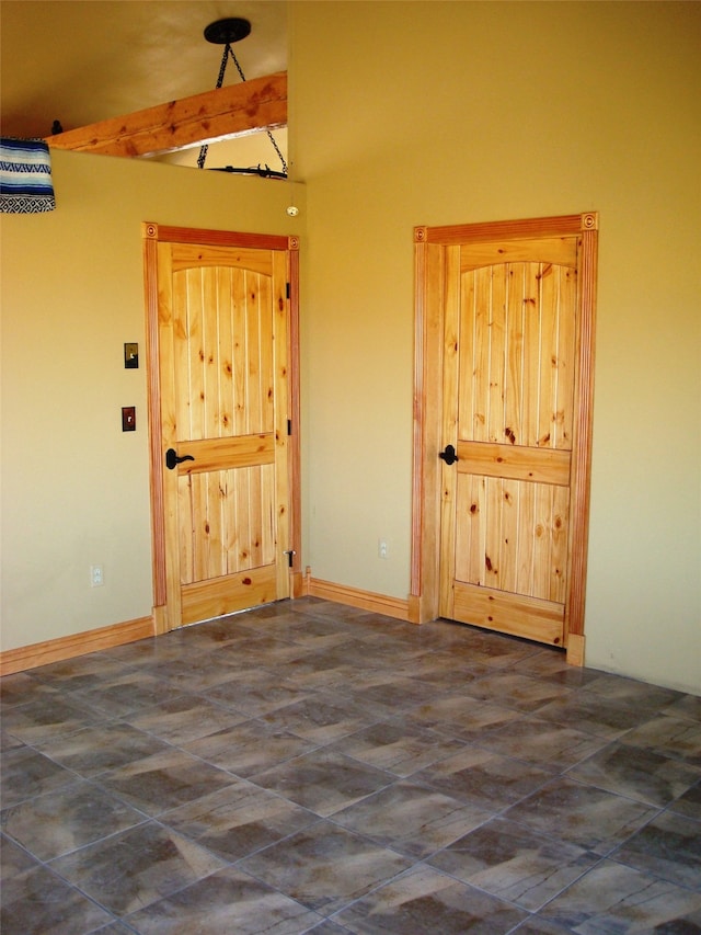 empty room with beamed ceiling and dark tile floors