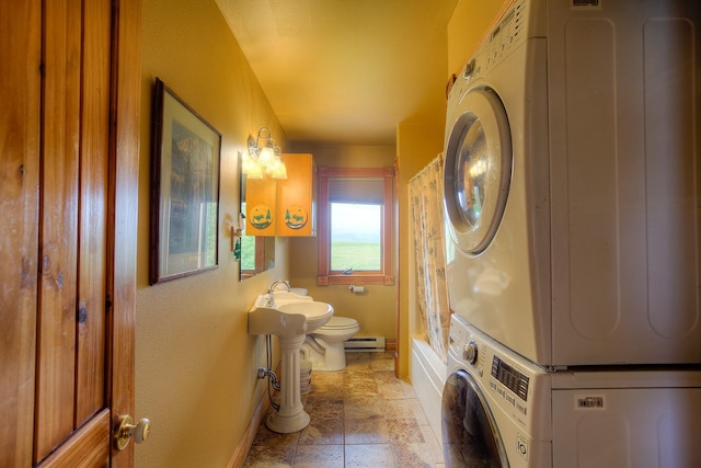 washroom featuring a baseboard heating unit, baseboards, stacked washer and clothes dryer, stone finish floor, and laundry area
