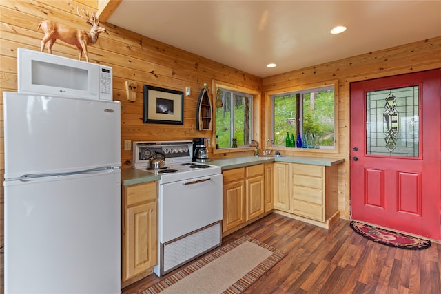 kitchen with light brown cabinetry, dark hardwood / wood-style floors, wood walls, sink, and white appliances