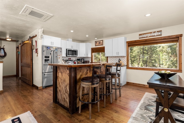 kitchen with a barn door, white cabinets, stainless steel appliances, and wood-type flooring