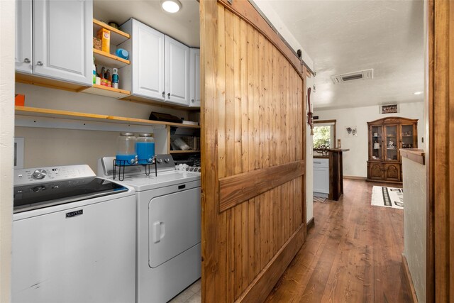 laundry room featuring hardwood / wood-style flooring, a barn door, cabinets, and washing machine and clothes dryer