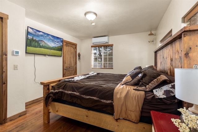 bedroom featuring a wall mounted air conditioner, wood finished floors, and baseboards