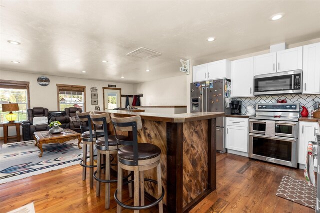 kitchen with white cabinetry, a center island with sink, dark hardwood / wood-style floors, and appliances with stainless steel finishes