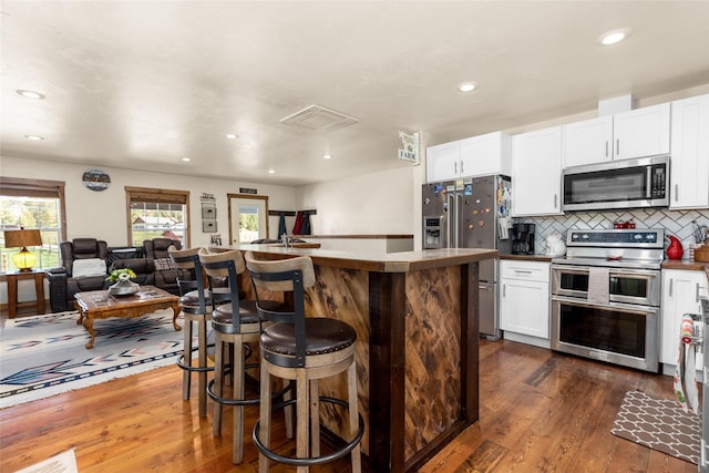 kitchen featuring dark wood finished floors, decorative backsplash, appliances with stainless steel finishes, open floor plan, and white cabinetry