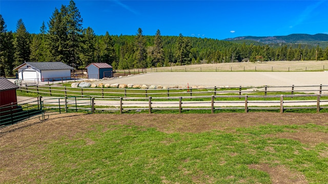 view of yard featuring an enclosed area, a mountain view, a wooded view, a rural view, and an outdoor structure