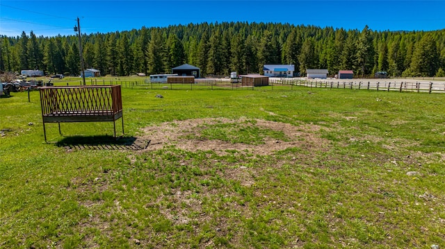 view of yard with fence, a wooded view, and an outdoor structure