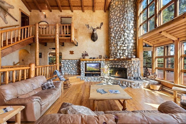 living room with hardwood / wood-style flooring, a stone fireplace, beamed ceiling, and a high ceiling