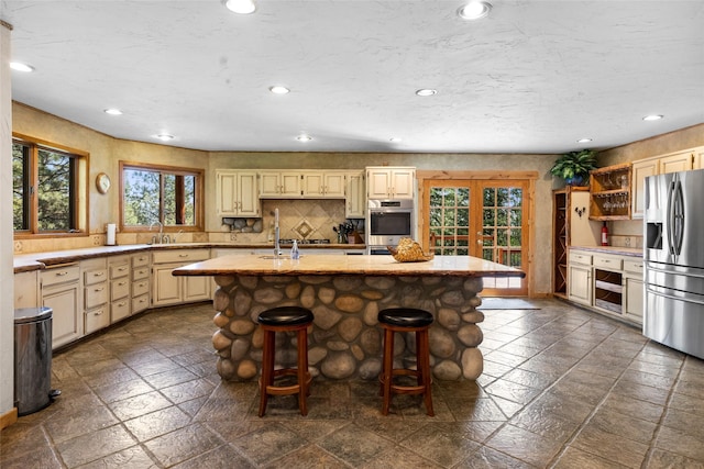 kitchen with a kitchen bar, backsplash, a kitchen island with sink, and appliances with stainless steel finishes