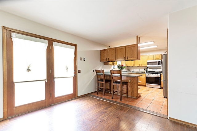 kitchen featuring light hardwood / wood-style flooring, kitchen peninsula, a kitchen bar, and stainless steel appliances