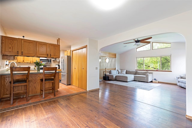 kitchen with stainless steel appliances, light hardwood / wood-style flooring, a breakfast bar, ceiling fan, and vaulted ceiling