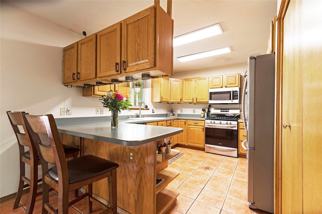 kitchen with kitchen peninsula, stainless steel appliances, light tile floors, sink, and a kitchen bar