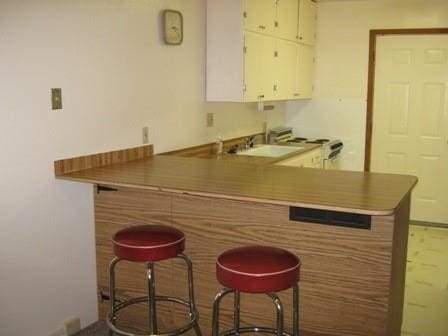 kitchen with kitchen peninsula, stove, sink, white cabinets, and a kitchen bar