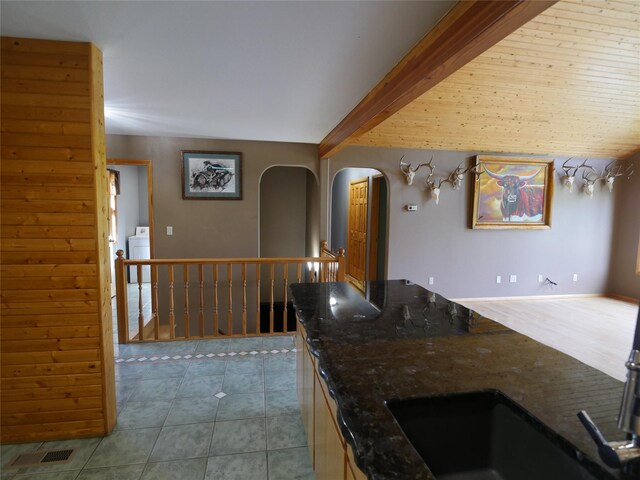 41698 Canal Rd, Polson, MT 59860 - kitchen featuring arched walkways, dark stone counters, washer / clothes dryer, light tile patterned floors, and beamed ceiling