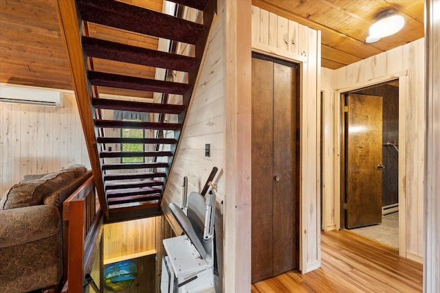 stairway with a wall unit AC, wooden walls, light hardwood / wood-style flooring, and a baseboard radiator