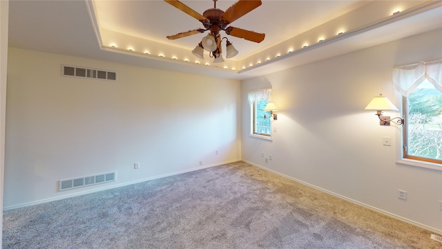 carpeted spare room featuring a wealth of natural light, ceiling fan, and a raised ceiling