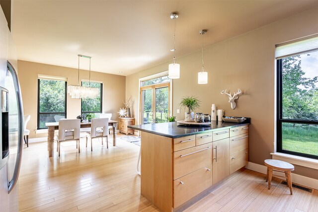 kitchen with stainless steel refrigerator, hanging light fixtures, light brown cabinetry, and light hardwood / wood-style floors