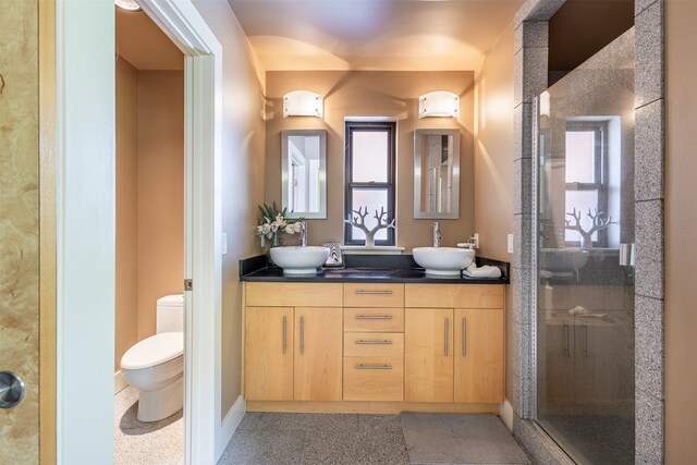 bathroom with a shower with door, double vanity, and toilet