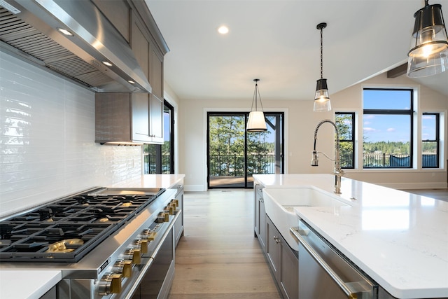 198 Blaine Lakeshore Dr, Kalispell, MT 59901 - kitchen with appliances with stainless steel finishes, wall chimney range hood, light wood-style flooring, decorative backsplash, and a sink