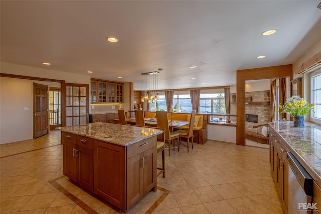 kitchen with decorative light fixtures, stainless steel dishwasher, a large fireplace, a kitchen island, and light stone countertops