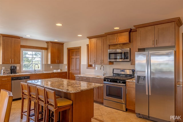 kitchen with sink, a breakfast bar area, stainless steel appliances, a center island, and light stone countertops