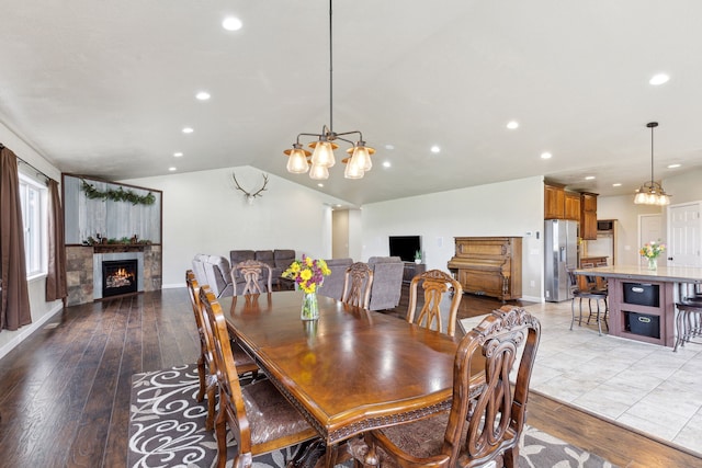 dining area with a chandelier, vaulted ceiling, light hardwood / wood-style flooring, and a tiled fireplace