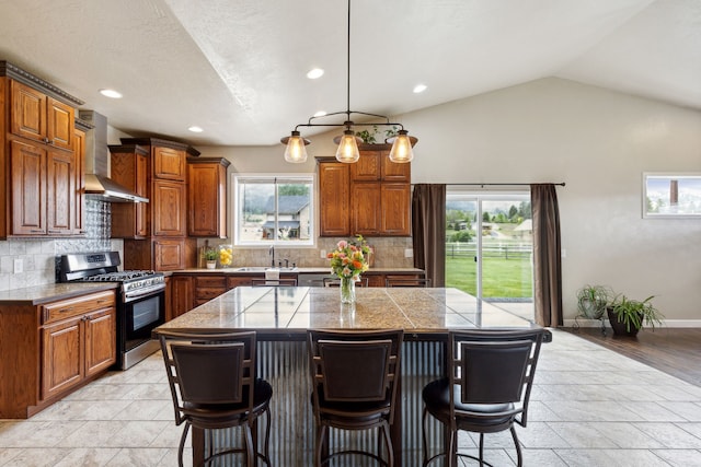 kitchen featuring a center island, stainless steel gas range oven, lofted ceiling, a kitchen breakfast bar, and wall chimney exhaust hood