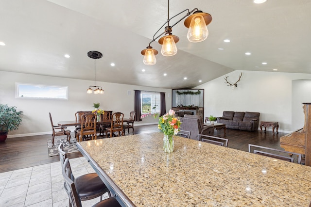 kitchen featuring a breakfast bar, a center island, lofted ceiling, light stone countertops, and decorative light fixtures