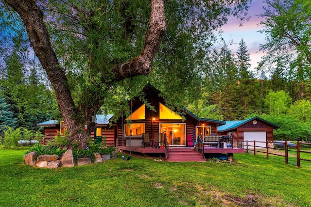 back house at dusk featuring a deck, a garage, an outdoor structure, and a lawn