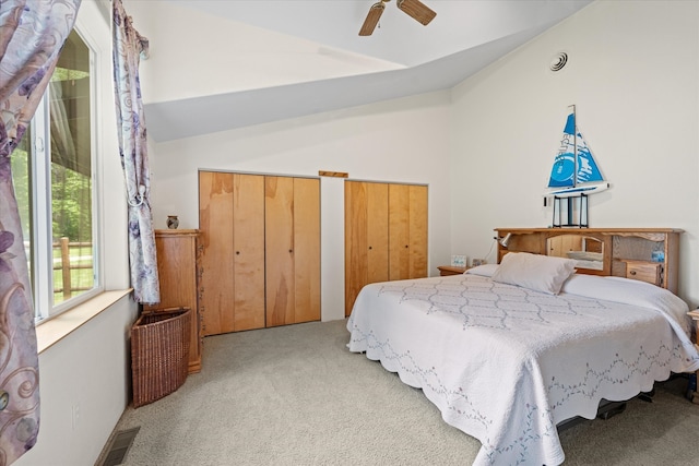 carpeted bedroom featuring multiple closets, ceiling fan, and vaulted ceiling