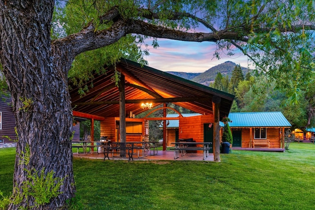 back house at dusk with a patio area, a lawn, a mountain view, and a gazebo