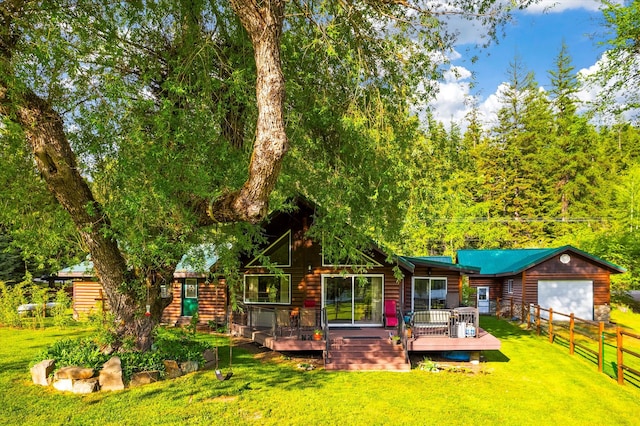 rear view of property featuring an outdoor structure, a garage, a lawn, and a wooden deck