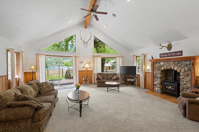 living room featuring a stone fireplace, beam ceiling, a healthy amount of sunlight, and carpet