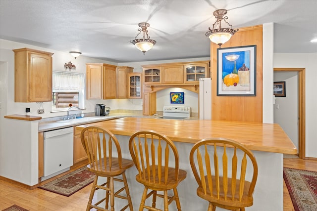 kitchen featuring decorative light fixtures, white appliances, sink, and light hardwood / wood-style floors