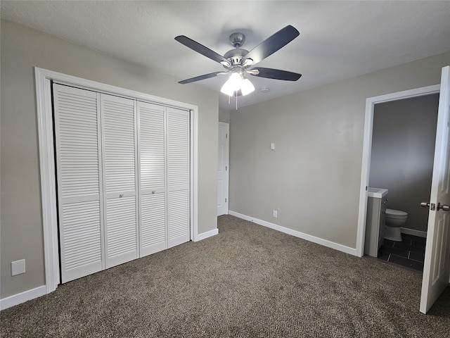 unfurnished bedroom with ceiling fan, dark colored carpet, a closet, and ensuite bath